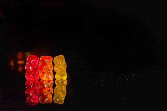 Gummy bears standing next to each other, isolated on a black background with reflection 