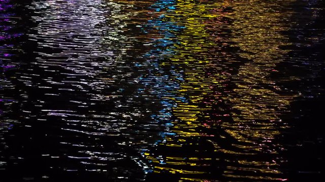 The night sea water waves reflects the bright street colorful light, close up