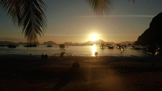sunset over the beach view through palm tree leaves. Sunset over the sea with islands and boats, Corong corong beach, Palawan, Philippines