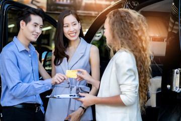 Salesperson working at car dealership.Young woman consultant and couple buyers signing contract for new car in auto show. Concept for car rental, sale.Paying credit card.