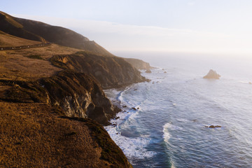 Aerial drone view of the Big Sur coastline in California. Beautiful golden light hitting the side of the cliffs at sunset along the coastal road. 