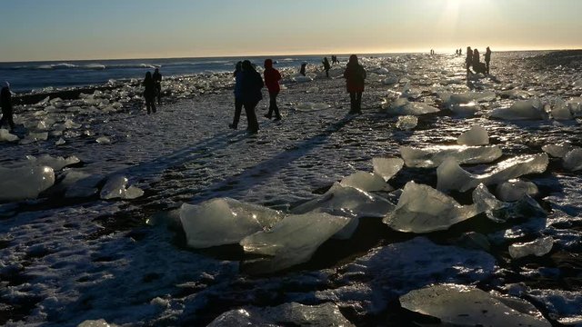 Silhouette unrecognizable people visiting iceberg ice chunks on black sand beach