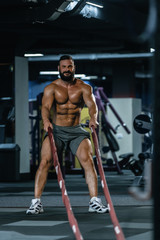 Obraz na płótnie Canvas Fit athletic bodybuilder pulling heavy battle rope
