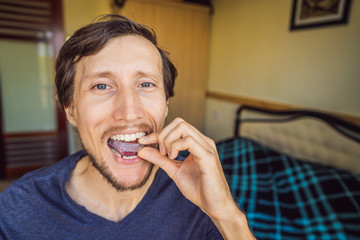Man placing a bite plate in his mouth to protect his teeth at night from grinding caused by...