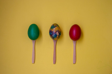 Three colorful eggs in wooden spoons isolated on yellow background, multicolored eggs, Easter tradition, celebration concept