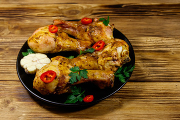 Roasted chicken drumsticks with spices in a black plate on a wooden table