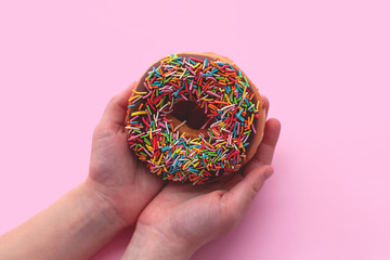 Classic chocolate donut with colorful sprinkles on pink background. Sweet dessert for holiday...