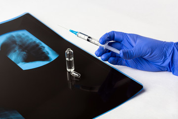Female doctor's hand in glove holds a syringe with vaccine against X-ray film (scan) of lungs....