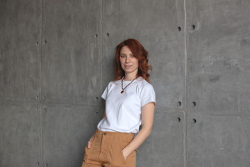 Young girl in a white T-shirt and beige pants. Concrete wall.