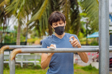 Man disinfects horizontal bar before sports. A man in a medical mask plays sports during the coronavirus epidemic