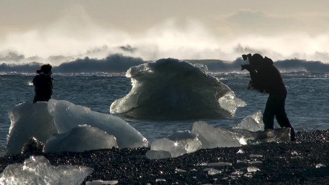 Model posing for photographer near iceberg ice floe broken from glacier with ocean waves in background