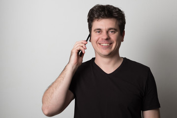 Man is talking on a cell phone. Smiling young man in a black T-shirt talking on the phone.