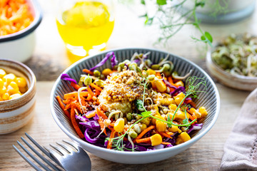 Vegetable salad of fresh red cabbage with carrots, onions, corn, mung seedlings in a plate on wooden background. Selective focus.