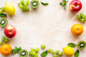 Fresh fruits background with citruses, apple, kiwi and grape on beige table top-down frame copy space