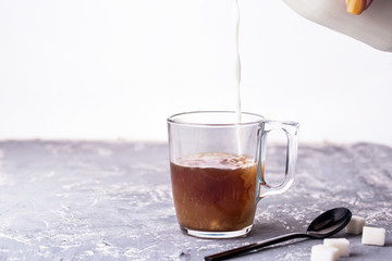 Coffee with milk in a glass cup, spoon, sugar, custard, a bottle of milk on a glass background.