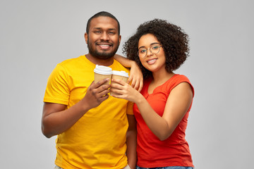 relationships and people concept - happy smiling african american couple with takeaway coffee cups over grey background