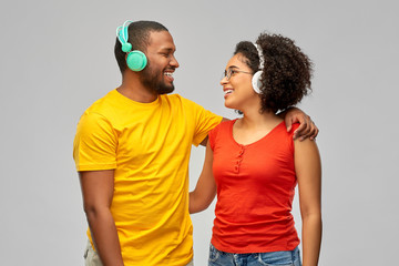 Fototapeta premium leisure, music and people concept - happy smiling african american couple with headphones over grey background