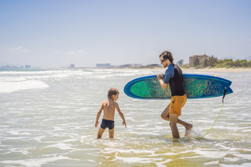 Father or instructor teaching his son how to surf in the sea on vacation or holiday. Travel and sports with children concept. Surfing lesson for kids
