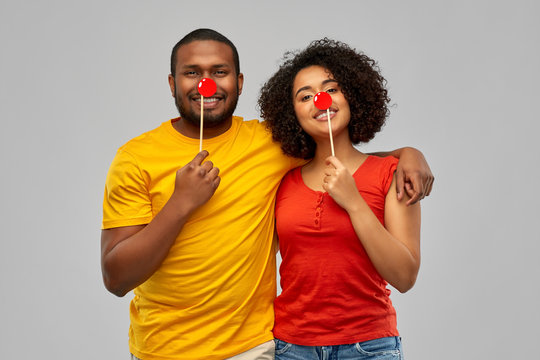 party, red nose day and people concept - happy smiling african american couple with clawn noses hugging over grey background