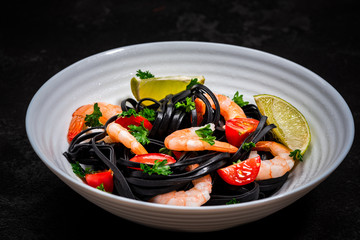 Black Pasta - Squid Ink, with Prawns, Seafood,Lemon and Tomatoes in White Bowl on  Dark Background. Top view.