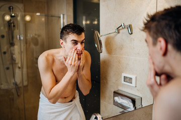 Young man having a shaving daily beard grooming routine,applying aftershave lotion.Allergic itchy...