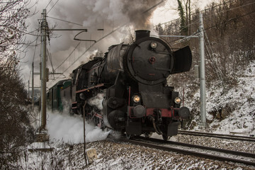 Front of the european style war train steam locomotive. German war locomotive built during the second world war rushing on the snowy train track, letting out steam and smoke.