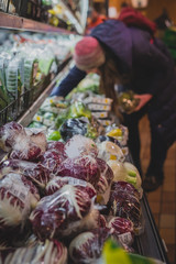 An unknown woman buying vegetables in a supermarket. Vertical photo of a woman in the background buying packed food in a fridge. Concept of healthy living, going vegan or vegetarian.