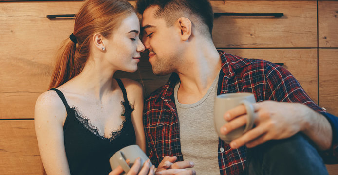 Cheerful caucasian couple in the kitchen drinking a coffee and kissing on the floor