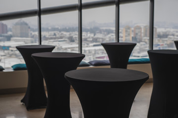Multitude of empty elegant black standing tables for lunch reception with a nice view behind over the city blocks.