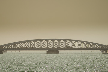 Faidherbe bridge, a metal bridge spaning over the river in Sant Louis, Senegal in an early hazy morning with a car and some people passing over it.
