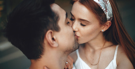 Lovely ginger woman with freckles kissing her lover while having a walk in the park