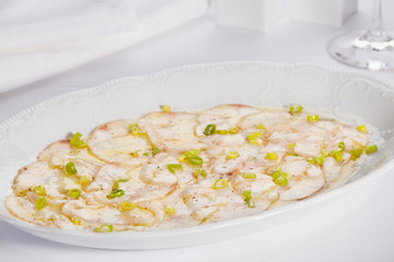 white fish carpaccio with greens on a white background