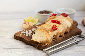 Cooked chicken breast in the oven, sliced on a wooden board. Served with chili pepper. Nearby are garlic, coarse salt, lime, peppercorns. Dietary nutrition.