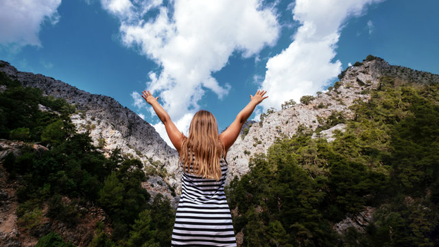 Happy blonde girl faceless look at mountain with hands up. Lifestyle, freedom, mental health concept. Stock photo.
