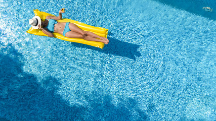 Beautiful young girl relaxing in swimming pool, woman swims on inflatable mattress and has fun in water on family vacation, tropical holiday resort, aerial drone view from above
