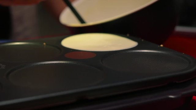 Pouring french pancake batter onto electric griddle stove at home to make small crepes, close up still shot