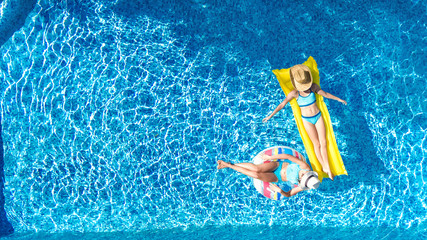 Children in swimming pool aerial drone view fom above, happy kids swim on inflatable ring donut and mattress, active girls have fun in water on family vacation on holiday resort
