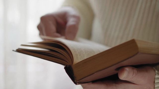 Man is reading old book, close-up with hands. Soft focus