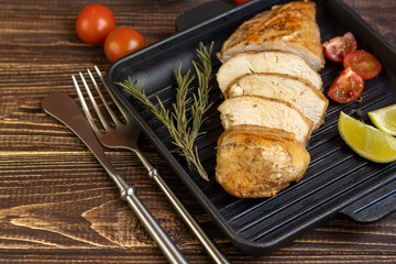 Cooked chicken breast in the oven in a grill pan. Nearby are cherry tomatoes, dry rosemary, lime, peppercorns. Dietary nutrition.