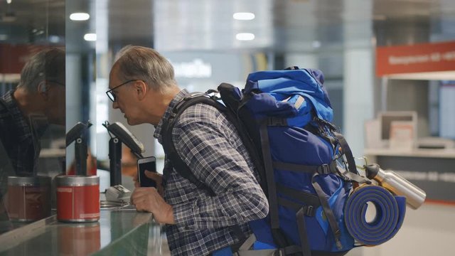 Backpack mature tourist purchasing train ticket in office paying with phone app