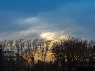 Sunset through clouds against the background of trees in the city