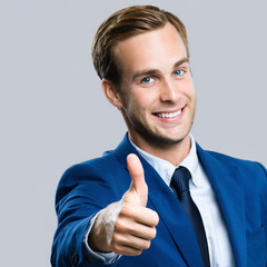 Portrait of happy smiling businessman showing thumbs up gesture, over grey background. Business success concept. Square composition.