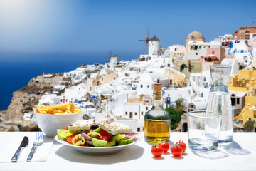 Fototapeta na wymiar Konzept der griechischen Küche mit Salat und Olivenöl vor der atemberaubenden Aussicht auf das Dorf Oia auf Santorini, Griechenland