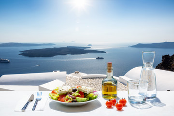 Traditionell Griechischer Salat mit Olivenöl vor der atembreaubenden Sicht auf die Kaldera in Santorini, Griechenland