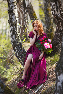red-haired girl in a burgundy dress walks in the forest