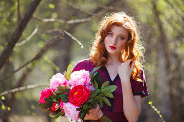 red-haired girl in a burgundy dress walks in the forest