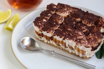 Tiramisu. Traditional italian dessert on a white background under concrete. Garnished with a sprig of mint, lime slices. In a transparent cup of tea.