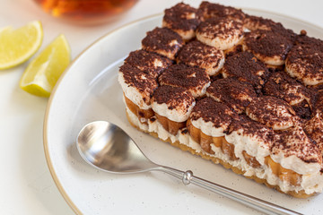 Tiramisu. Traditional italian dessert on a white background under concrete. Garnished with a sprig of mint, lime slices. In a transparent cup of tea.