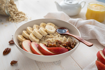 healthy breakfast bowl. oatmeal with banana, peach, pecans on a white, wooden background