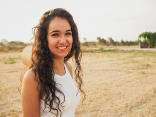smiling and happy brunette beautiful woman with white shirt standing on the field with hay bales in...